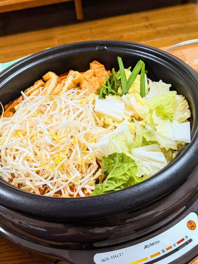 鍋にもやしや白菜、油揚げなど具材たくさん入っている様子